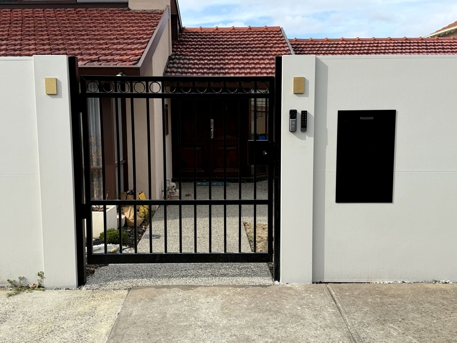 A black pedestrian gate between EstateWall piers, with a video intercom, keypad and parcel box set into the wall, Camberwell.