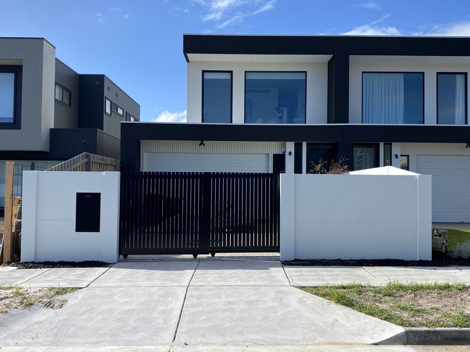 Chelsea frontage in daylight: white VogueWall on either side of a closed black telescopic sliding gate, with a black parcel box set into the wall.