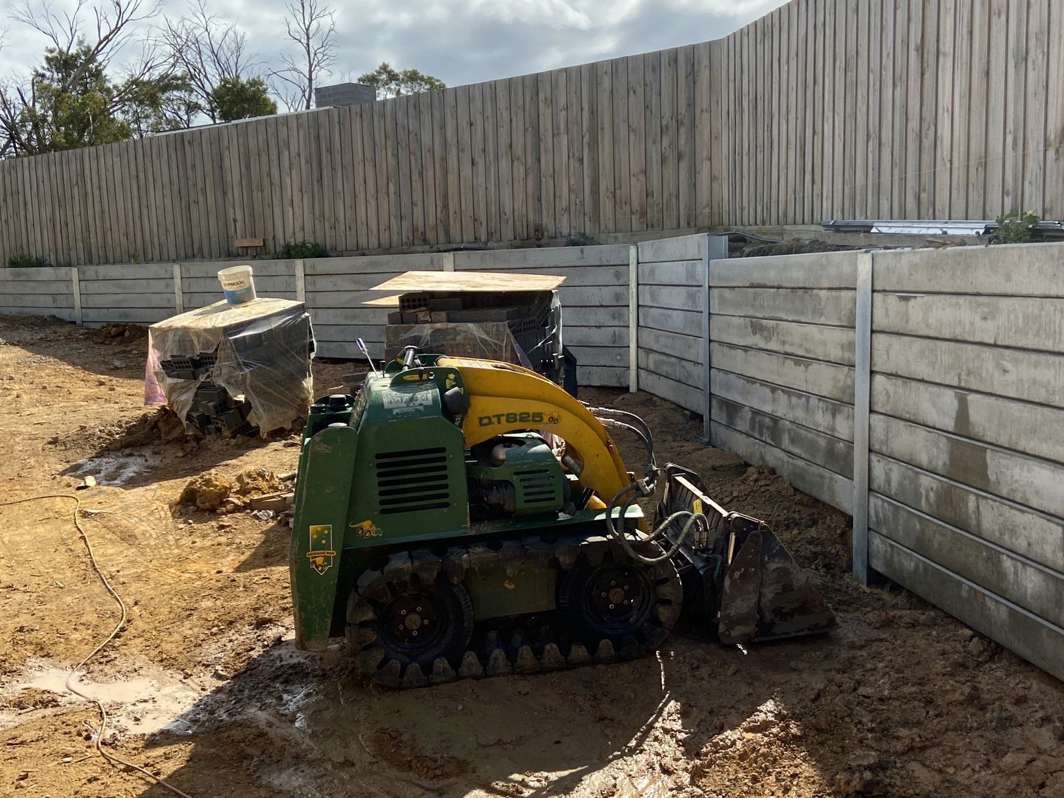 Sleeper retaining walls at two levels on the Mount Eliza site during construction, with a tracked loader in front.