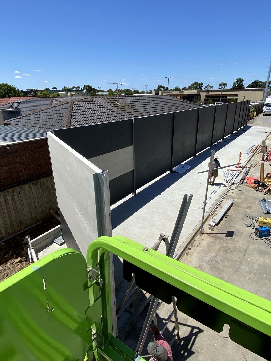 Point Cook during installation, seen from a work platform: charcoal acoustic panels running between the loading dock and the roofs of the neighbouring houses.
