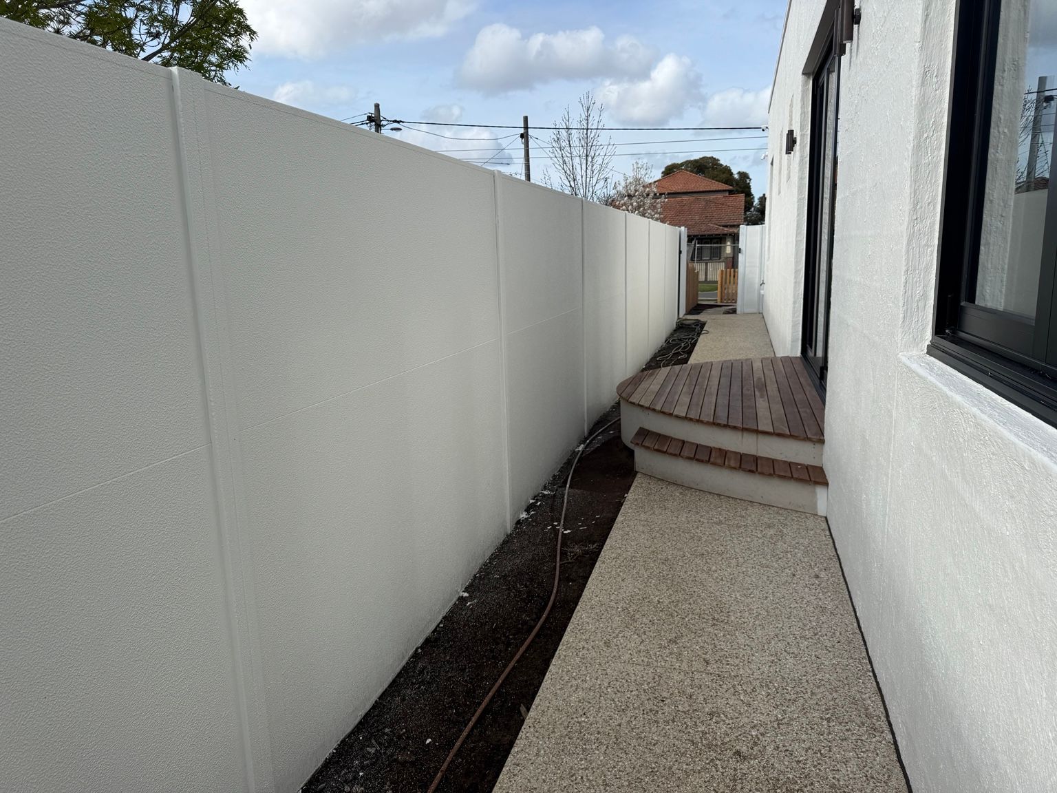 A white SlimWall side boundary running beside a house and a timber deck, Reservoir. A modular wall project, not an acoustic wall.